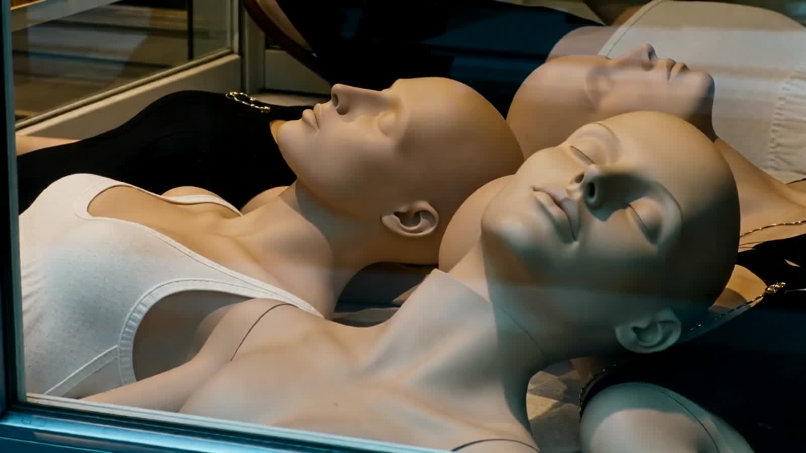 Mannequins without any accessories are laying on the shop window. Suddenly one of them is turning its head towards the v...