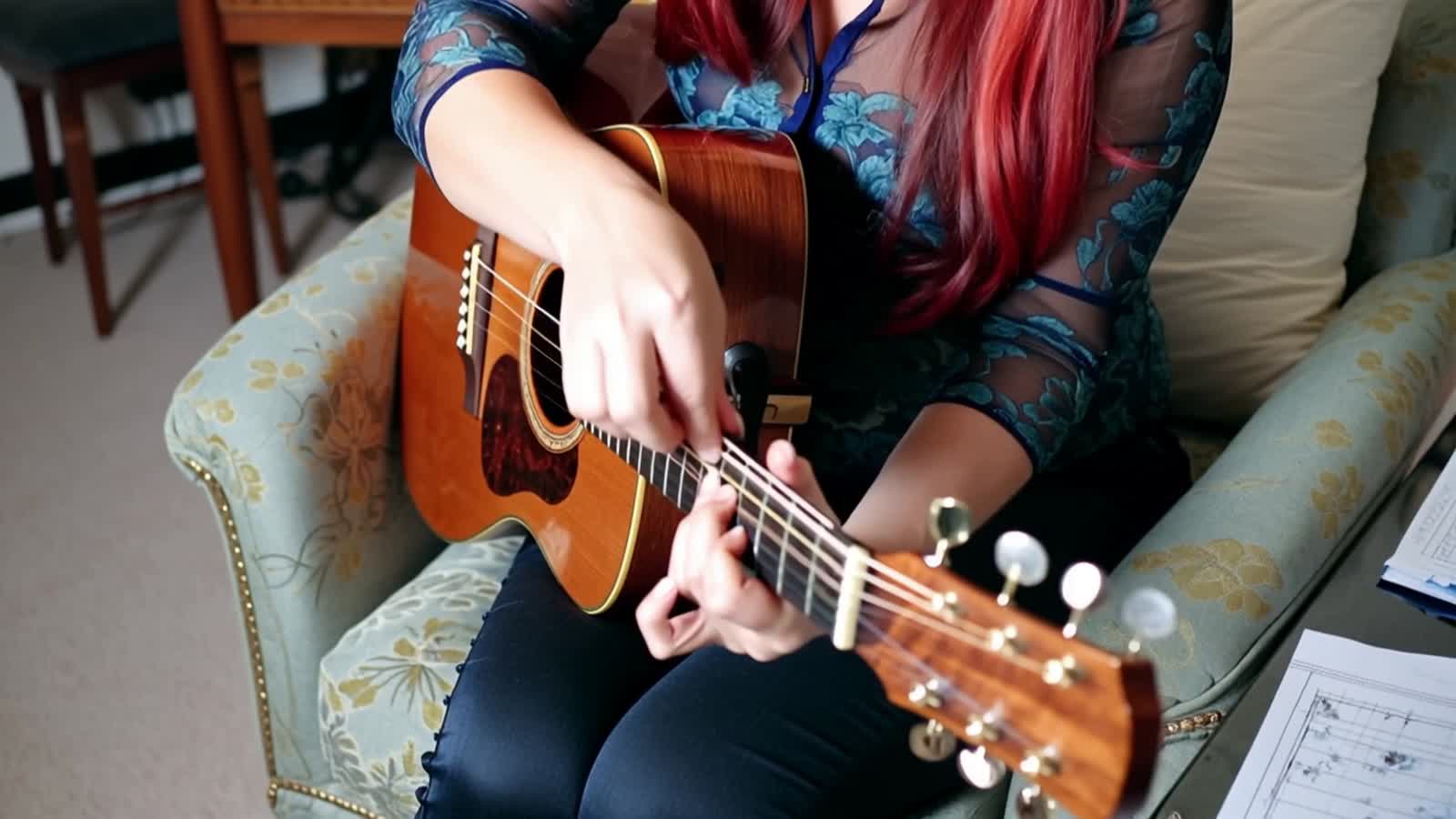 A redhaired woman sitting on a Paisely pattern armchair changing guitar strings