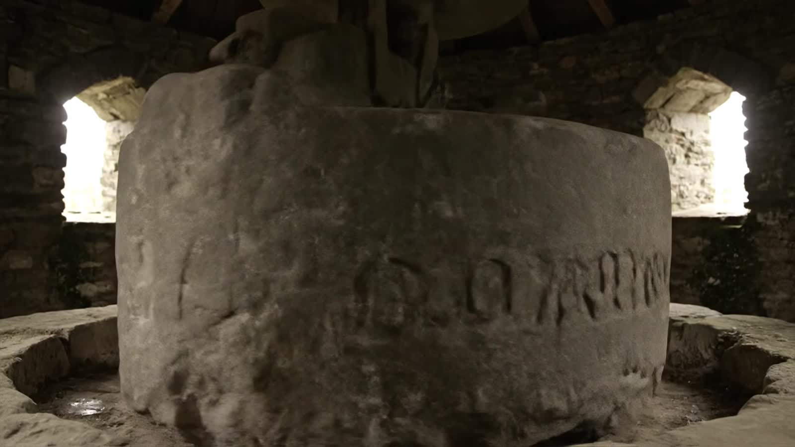 A massive grind stone in a tiny round old medieval time grinding mill with the words "OLD BONEGRINDER" etched in the sid...