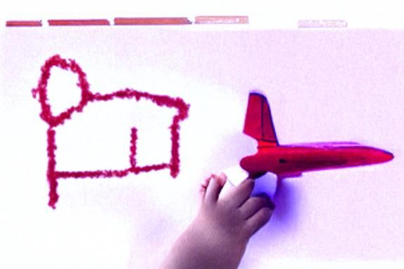 4-year-old boy draws a airplane with a red crayon on a white...
