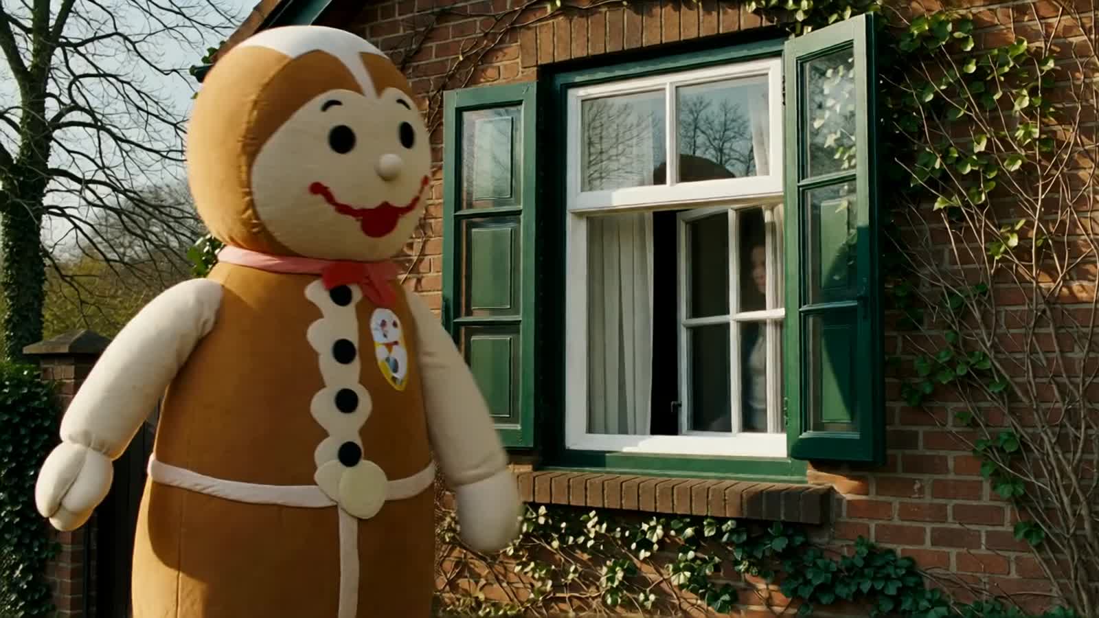A huge gingerbread doll made of light-colored fabric, with button eyes and an embroidered mouth is outside the building,...