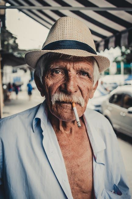 Old man with a moustache wearing a hat and smoking a cigarette