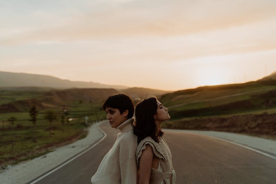"A scenic view where a paved road splits into two distinct paths forming a Y shape, with two people standing in the middle, one road needs t...
