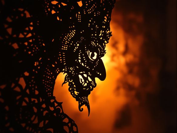 A detailed Wayang Kulit character design, inspired by traditional Indonesian shadow puppetry art, featuring intricate leatherwork and a dramatic silhouette against a warm, glowing backdrop.