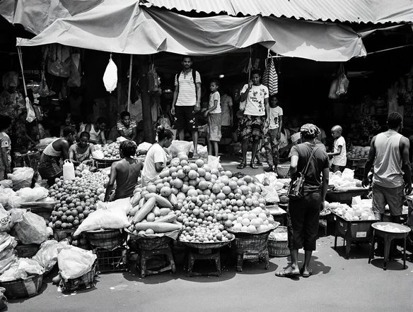A black and white photograph of a bustling marketplace in a developing country, captured in a candid, documentary style, with sharp focus and natural lighting.