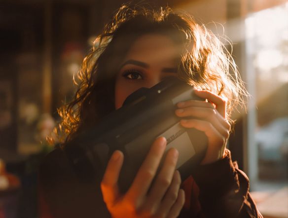 A portrait of a person holding a vintage camcorder, bathed in soft, warm light. The image exhibits noticeable old school video grain and a deeply nostalgic VHS look, complete with subtle color bleeding.