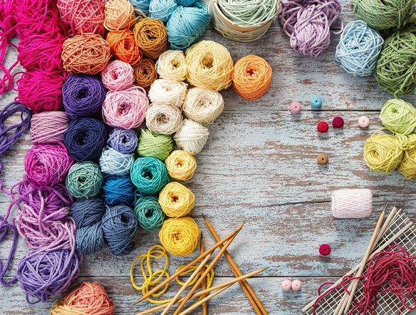 A vibrant array of yarn spools in a rainbow of colors, arranged artistically on a wooden table with knitting needles.
