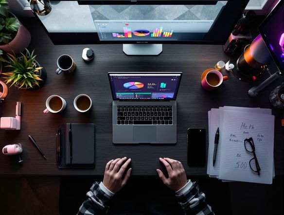 Overhead shot of a modern office desk with a vibrant pie chart displayed on a laptop screen, surrounded by coffee cups, notebooks, and stylish office supplies.