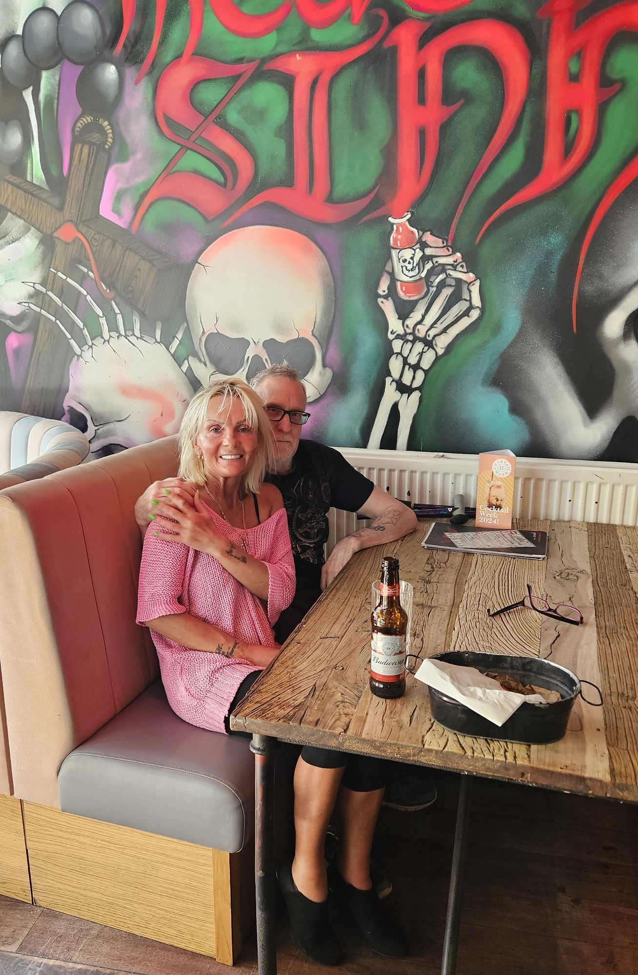 attractive young nun with man smiling directly at camera, skulls painted on wall behind hyperdetailed charcoal drawing