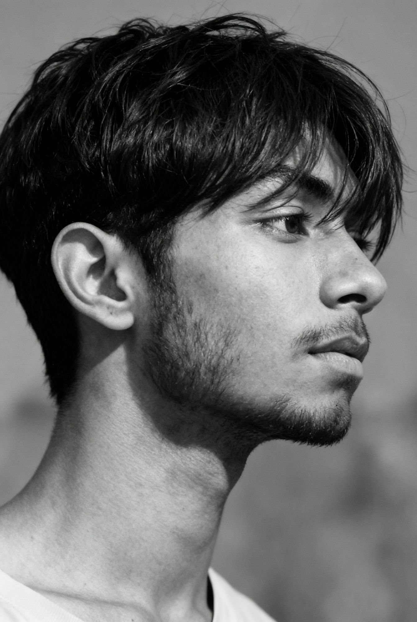 Create a black and white, close-up side profile portrait of a young man with wavy hair covering part of his forehead, looking to the right. ...