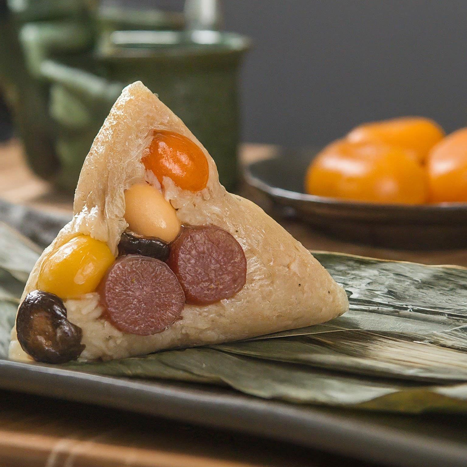 A close-up photo of a zongzi , a pyramid-shaped rice dumpling with sliced chinese sausage , Shitake, salted cured egg yolk , ginko seed , ta...
