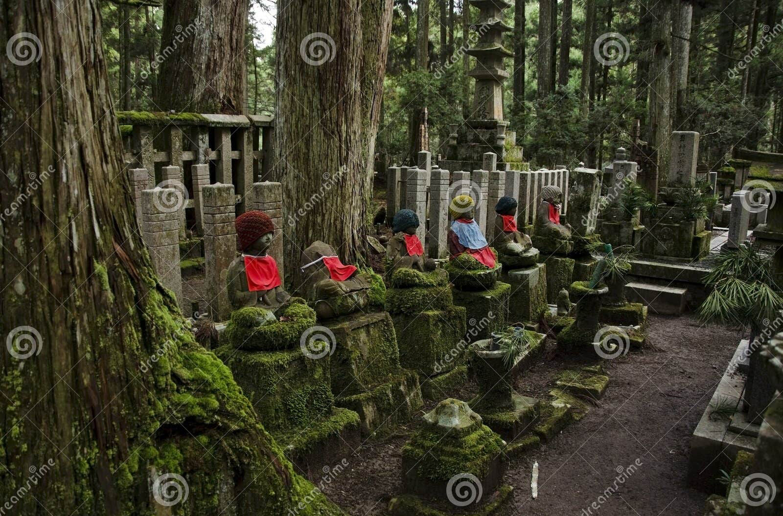 A japanese graveyard with stone lanterns and a statue of buddha, with japanese maples with red leaves in the background in a photographic st...
