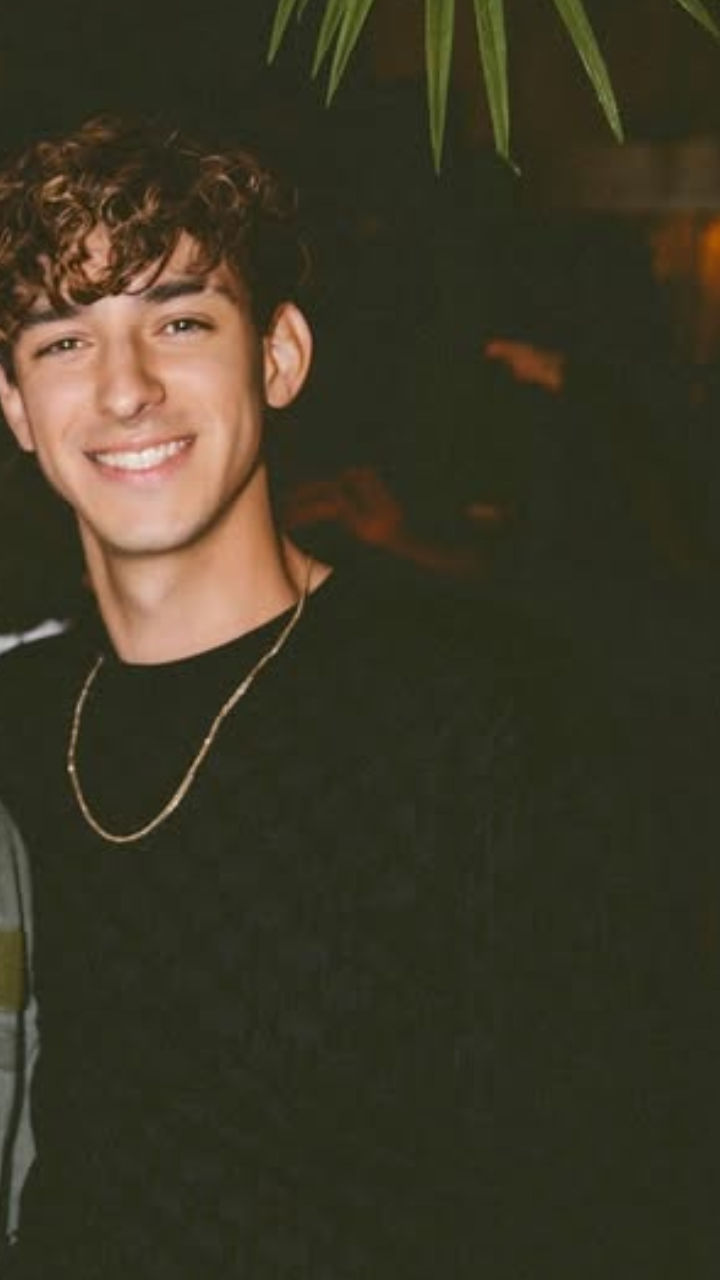 Create an image of a very tall young European knight with big eyes, dressed in entirely black armor, kneeling on a stormy beach at sunrise, ...