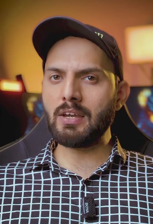 sitting on a light wooden chair in a dimly lit room, wearing a relaxed black hoodie and dark pants. the light source comes from a window wit...