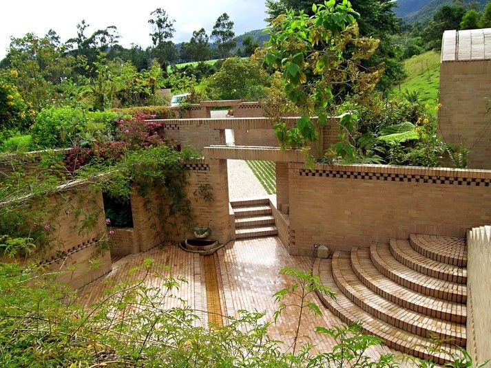 Outdoor space designed by Rogelio Salmona, sliding, with natural and floral plants, brick, calm and natural atmosphere, vines, wall fountain...