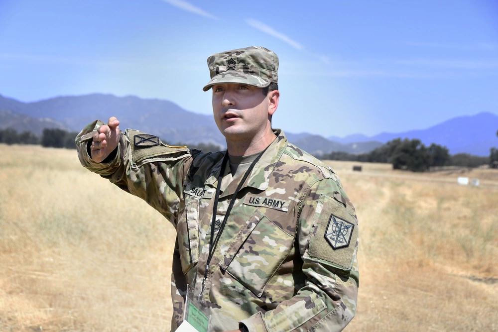 female army instructors pointing at A-10 Warthog, holding a clipboard, field cap, goggles, sidearm