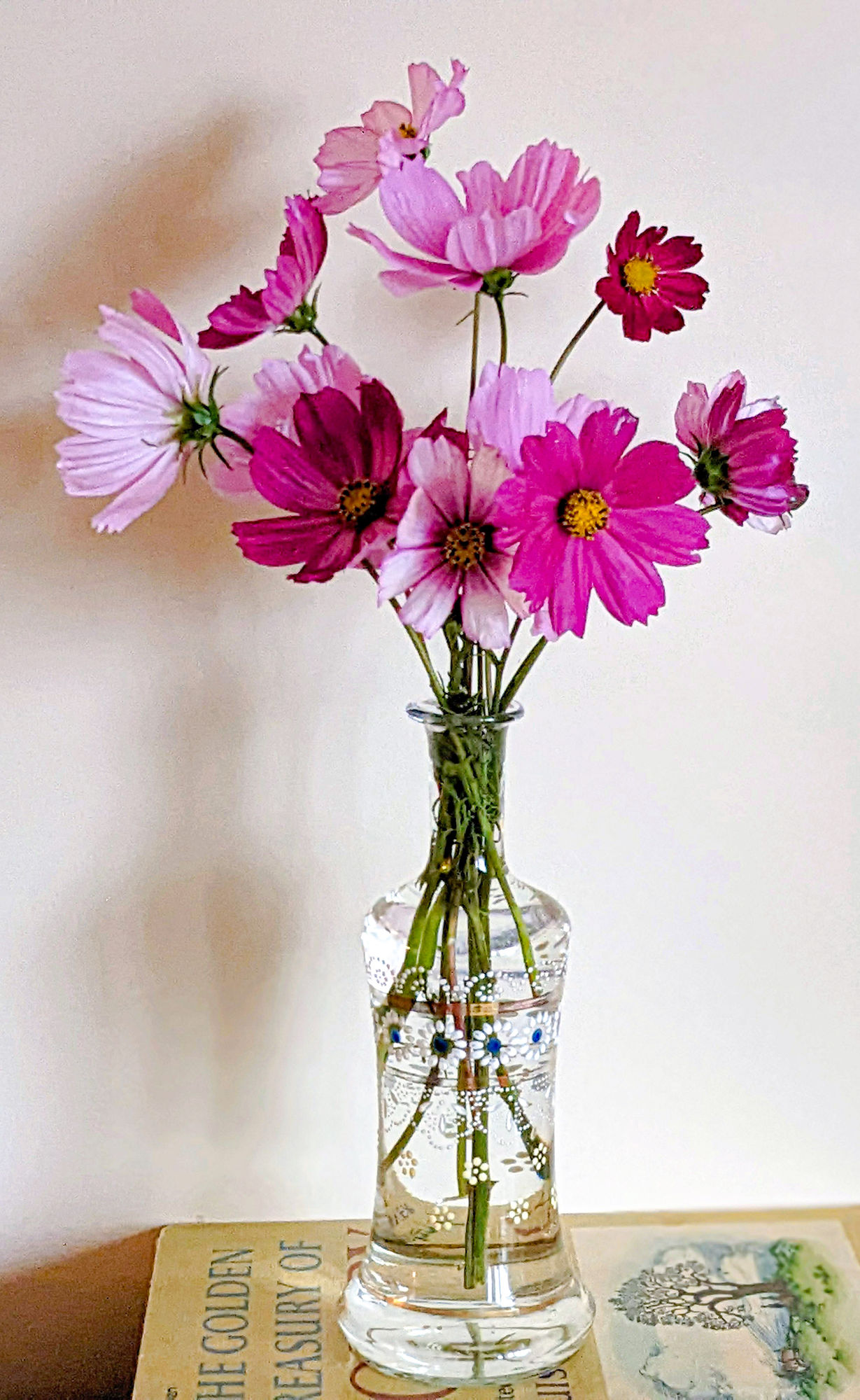 Vintage glass vase holding a small bouquet of cosmos flowers.