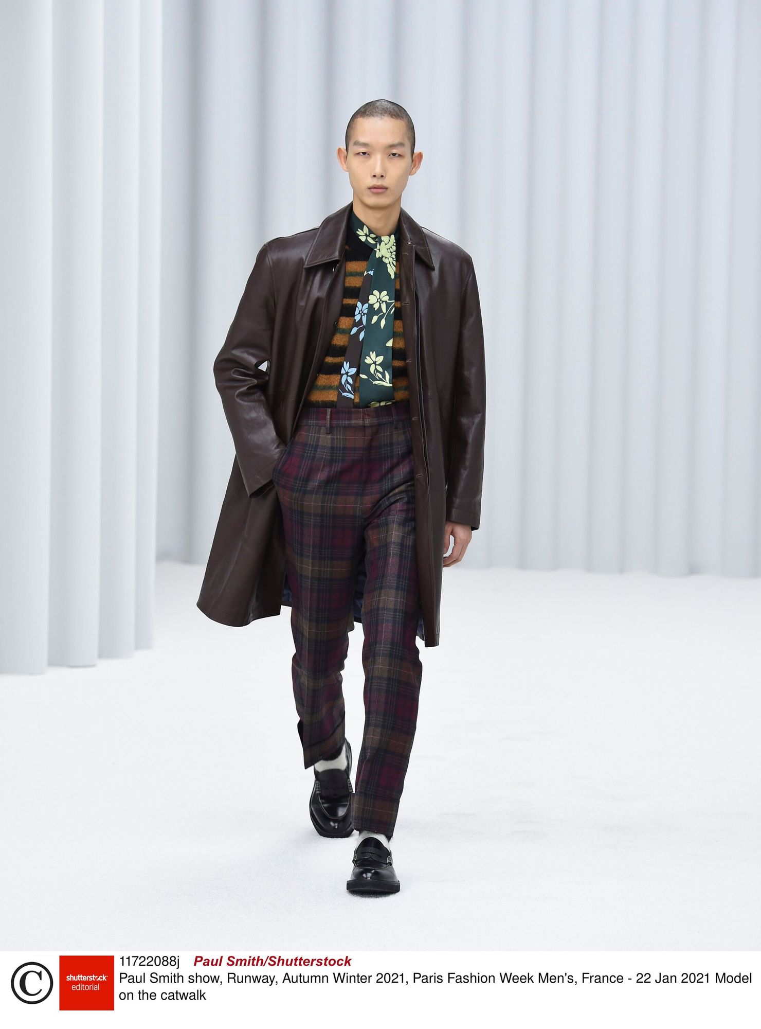 A young man in his thirties, long black hair, a slight smile, a full body, fully clothed, a sea bay and a ship in the background