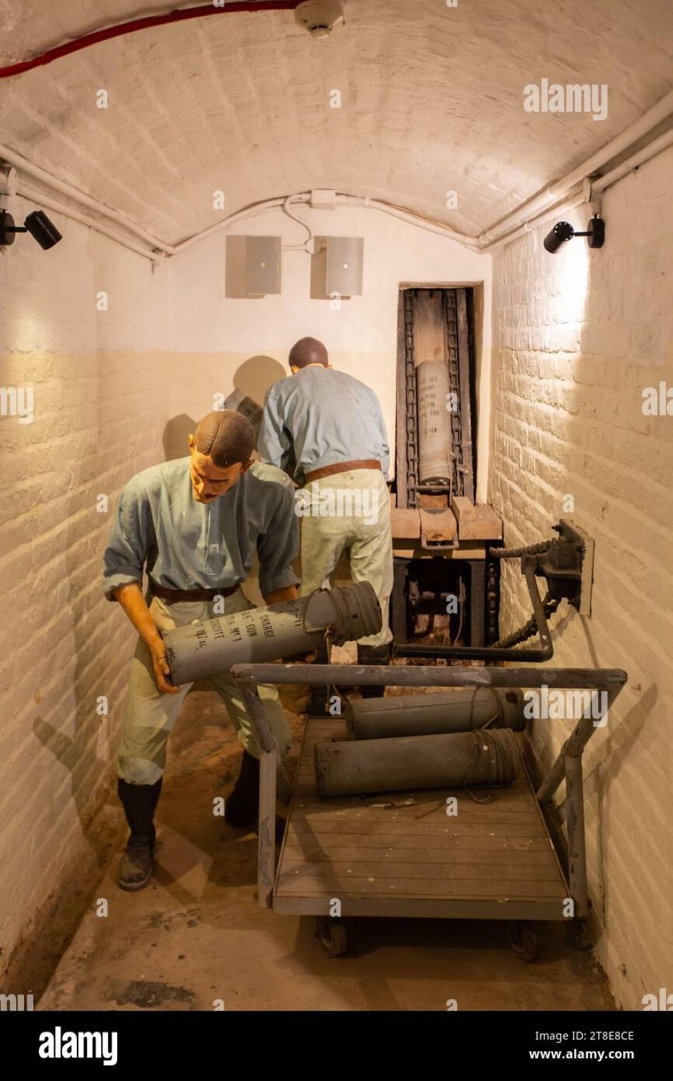 2 British Caucasian soldiers based in Singapore in the 1900s, in passageway of underground magazine, placing cartridge onto hydraulic hoist,...