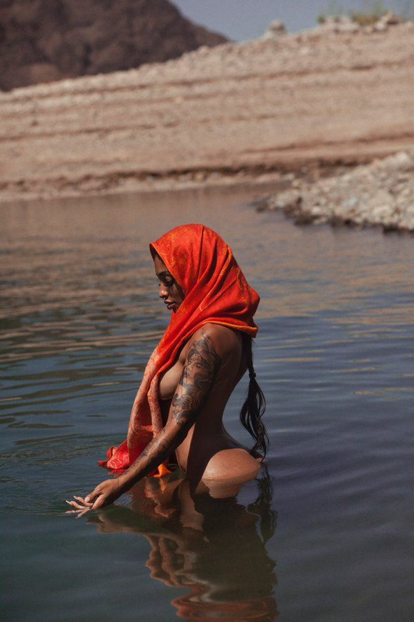 ,A young woman with dark skin wearing a red headscarf sitting in a body of water