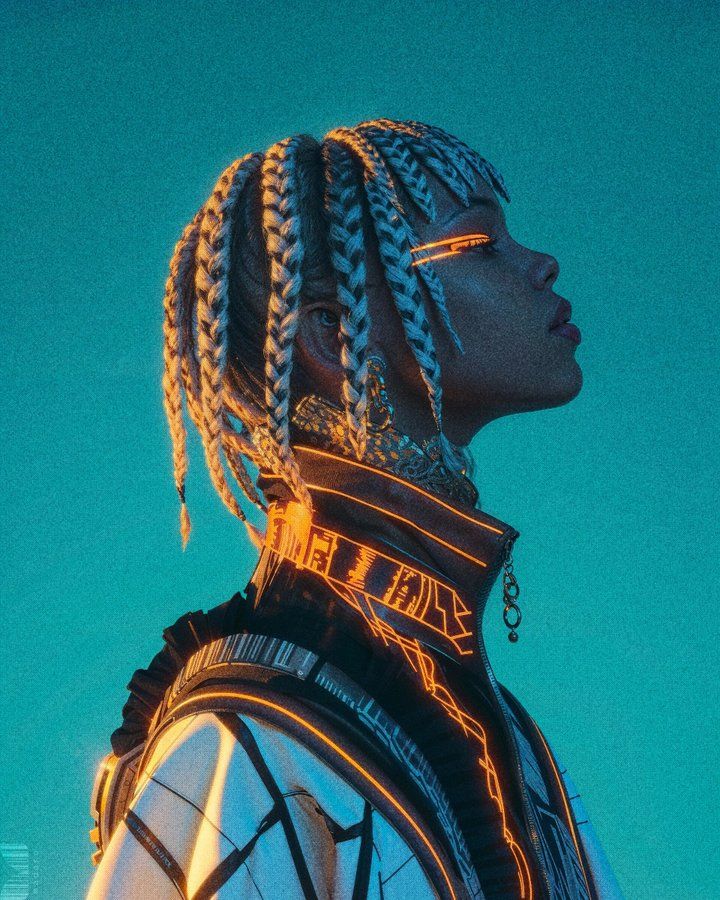 A young Black woman with long braided hairstyle, wearing colorful traditional African clothing and jewelry against a teal background