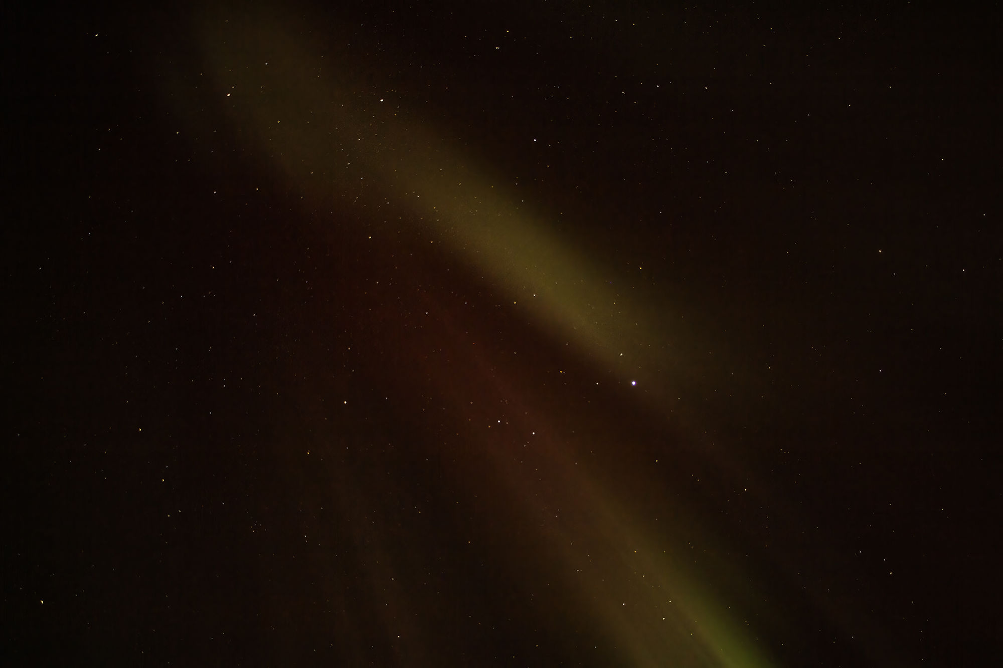 A grey haired senior woman sitting on a bench with a coffee watching the northern lights that she sees overhead