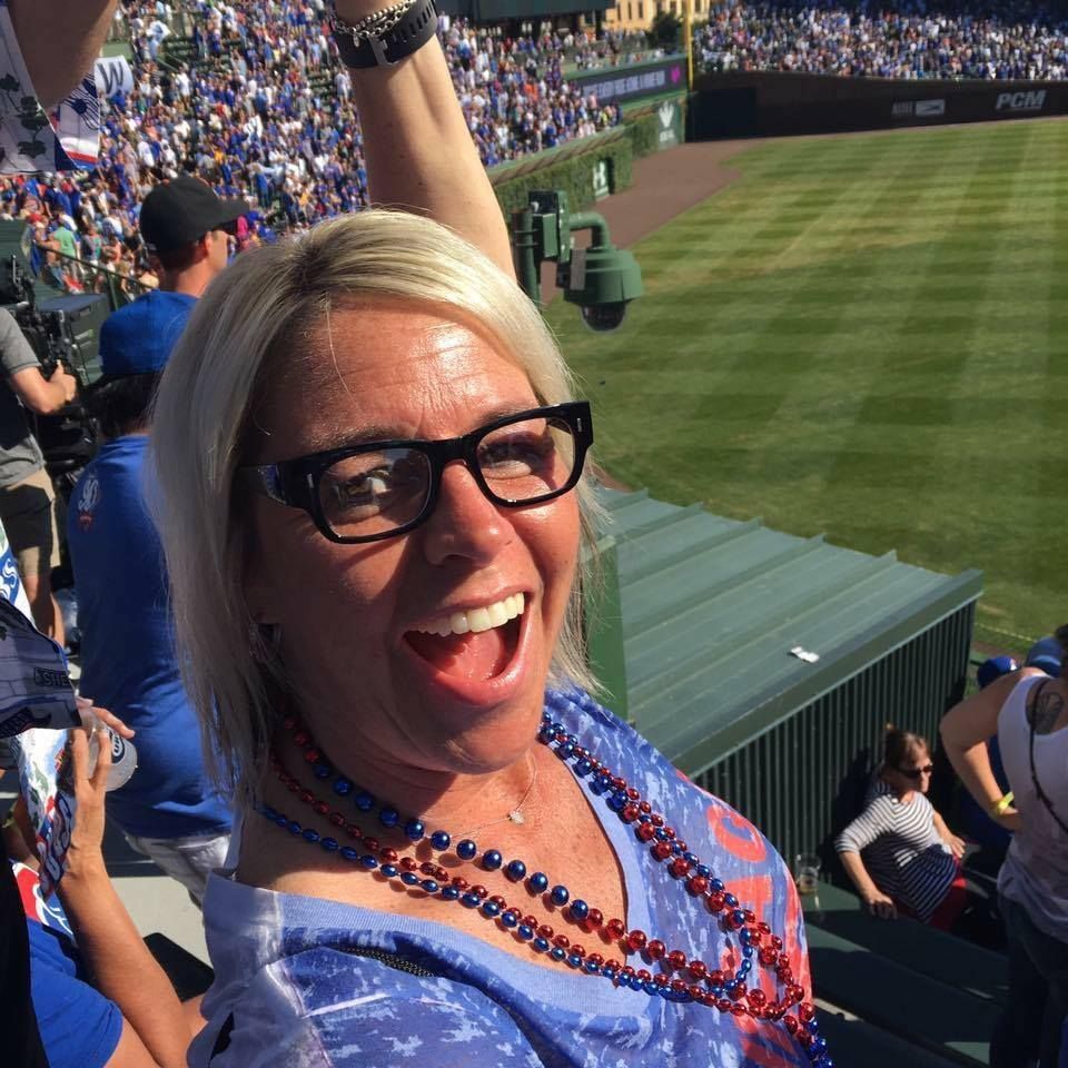 "Fun at the Ballpark 1"<lora:Color The Unexpected:1.0> Blonde Haired woman 40s waering brown squared top frame glasses in stands of Wrigley field wearing a Cubs ti...