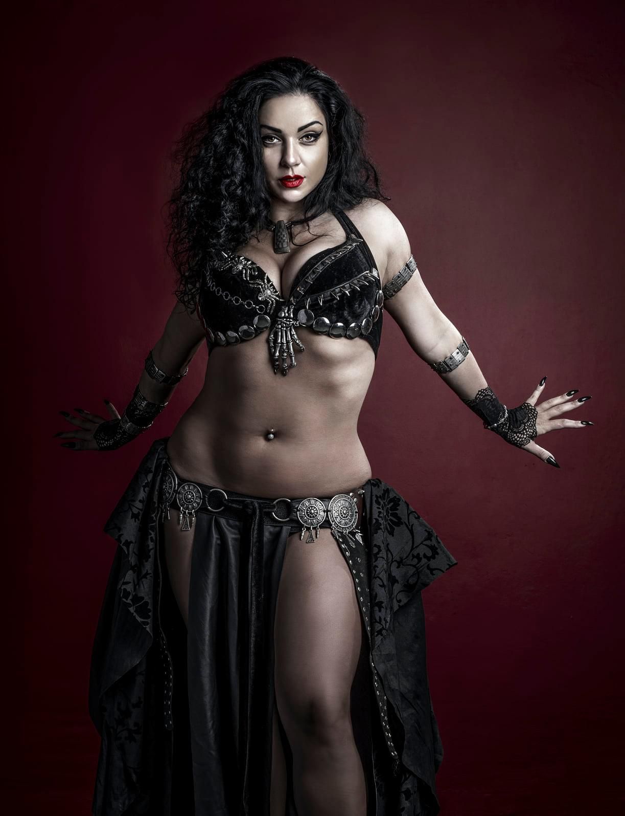 A captivating, cinematic portrait of a witch featuring a woman with cascading dark curly hair and an array of intricate tattoos. She dons si...