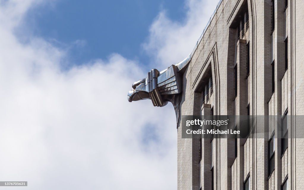 A gleaming chrome gargoyle  on top of a modern glass skyscraper