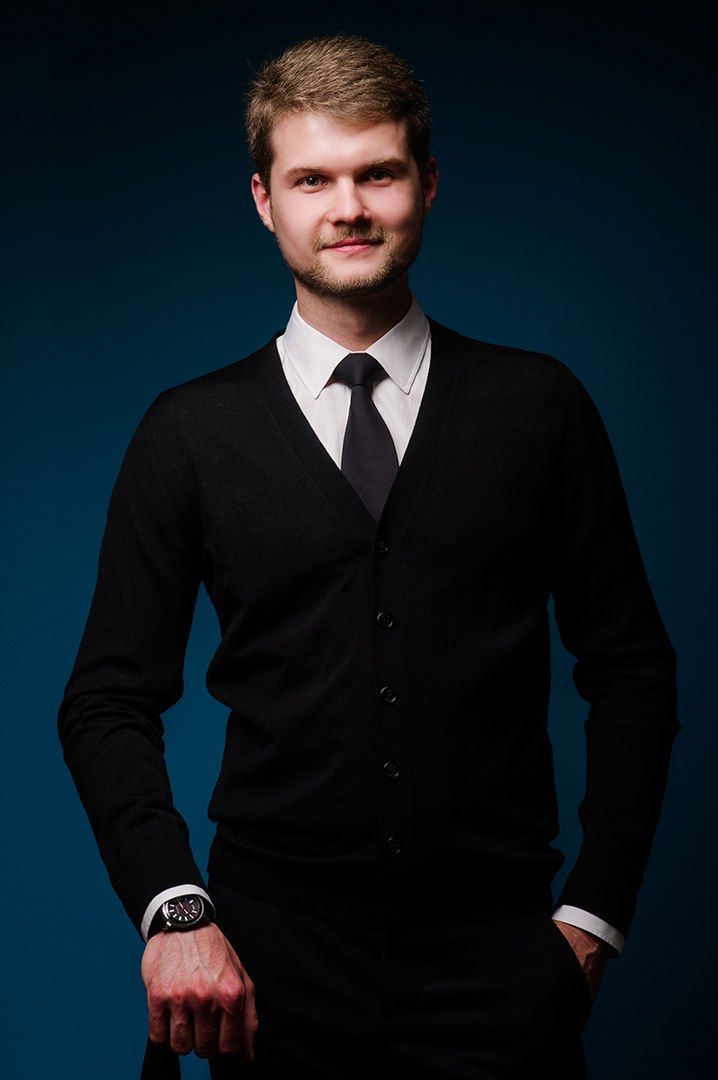 A warm, cozy indoor scene features a man sitting on a white chair, leaning forward, with a serene and calm expression. He wears a white chun...