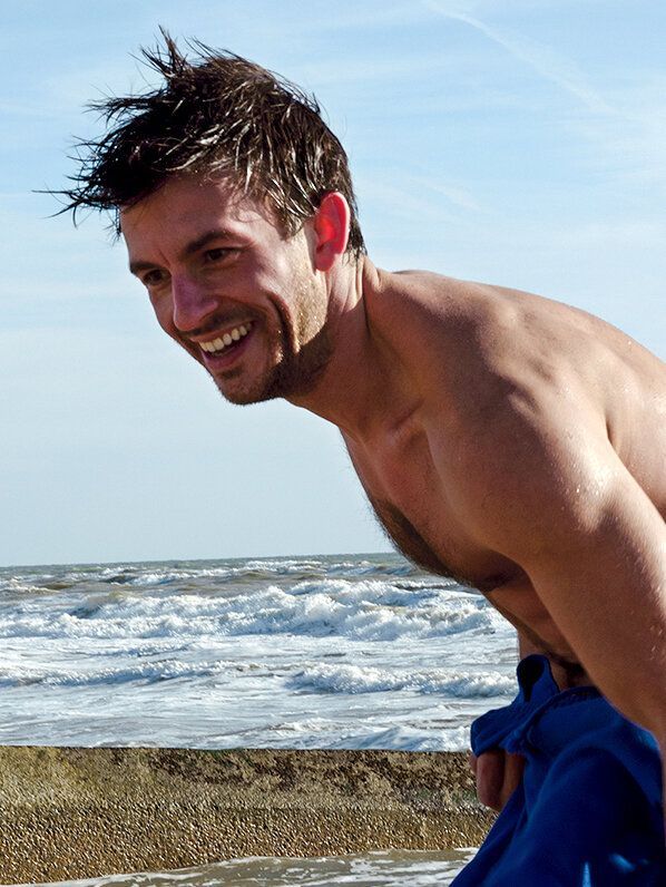 <lora:Murraypunk Flux:1.0> <lora:Detailed realism:1.0> <lora:SuperHyperrealismFlx:1.0> A smiling man with dark, wet hair stands on a beach, ...