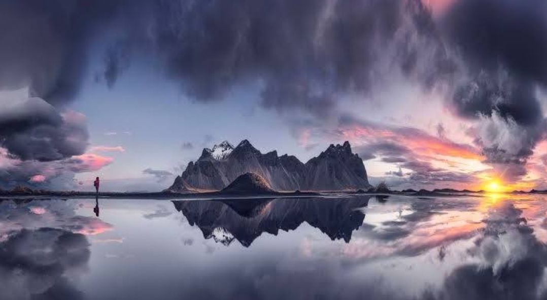 A 4K, 3:4 aspect ratio, photorealistic image of a lone figure in a red coat standing on a dark, reflective beach. In the background, jagged,...