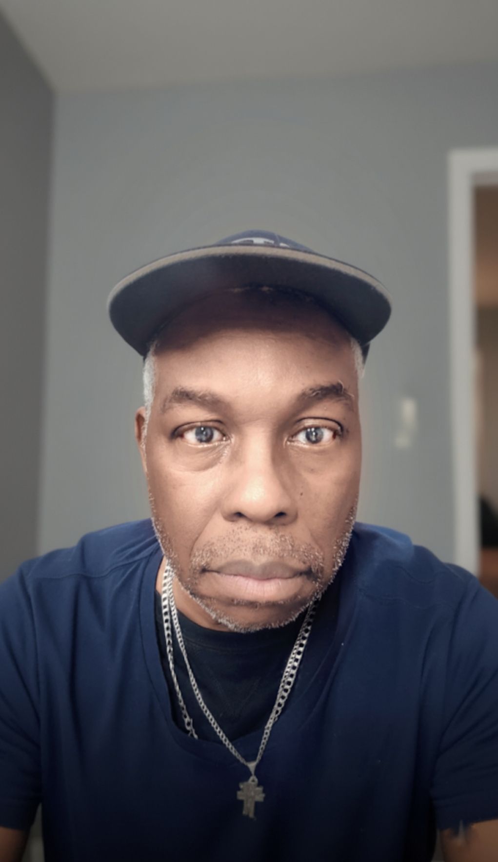 ​A close-up, centered portrait of a middle-aged Black man looking directly at the camera with a neutral, serious expression.
​He has salt an...