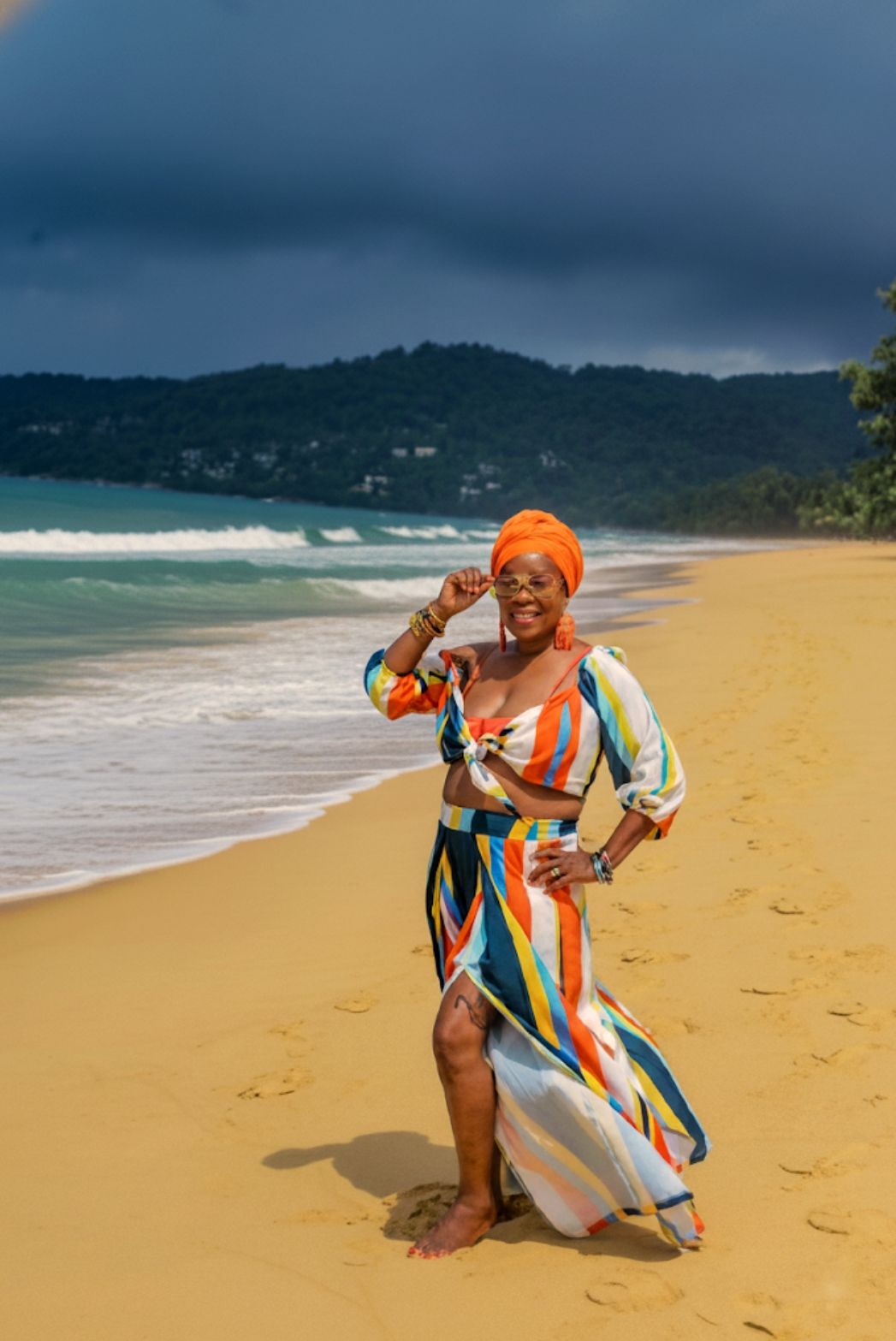 A vibrant, ultra photorealistic cinematic outdoor shot on a Samsung Galaxy S25 FE features a woman standing confidently on a golden sandy be...