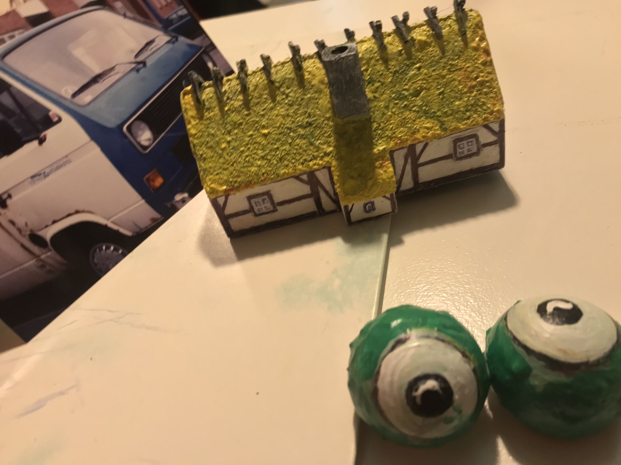 A photo of a decaying car with blue front and white rusty mid and back section. A miniature half-timbered Tudor house farm with thatched roo...