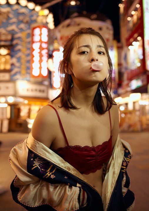 a Christmas girl show her shoulder and standing on the street at night. red color clothes, long hair, chewing bubble gum.
