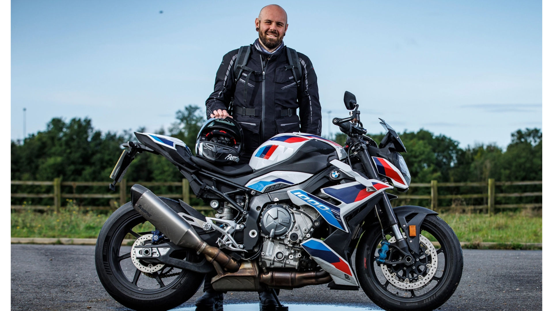 A werewolf biker wearing sports biker gear stands next to a bmw m 1000 r