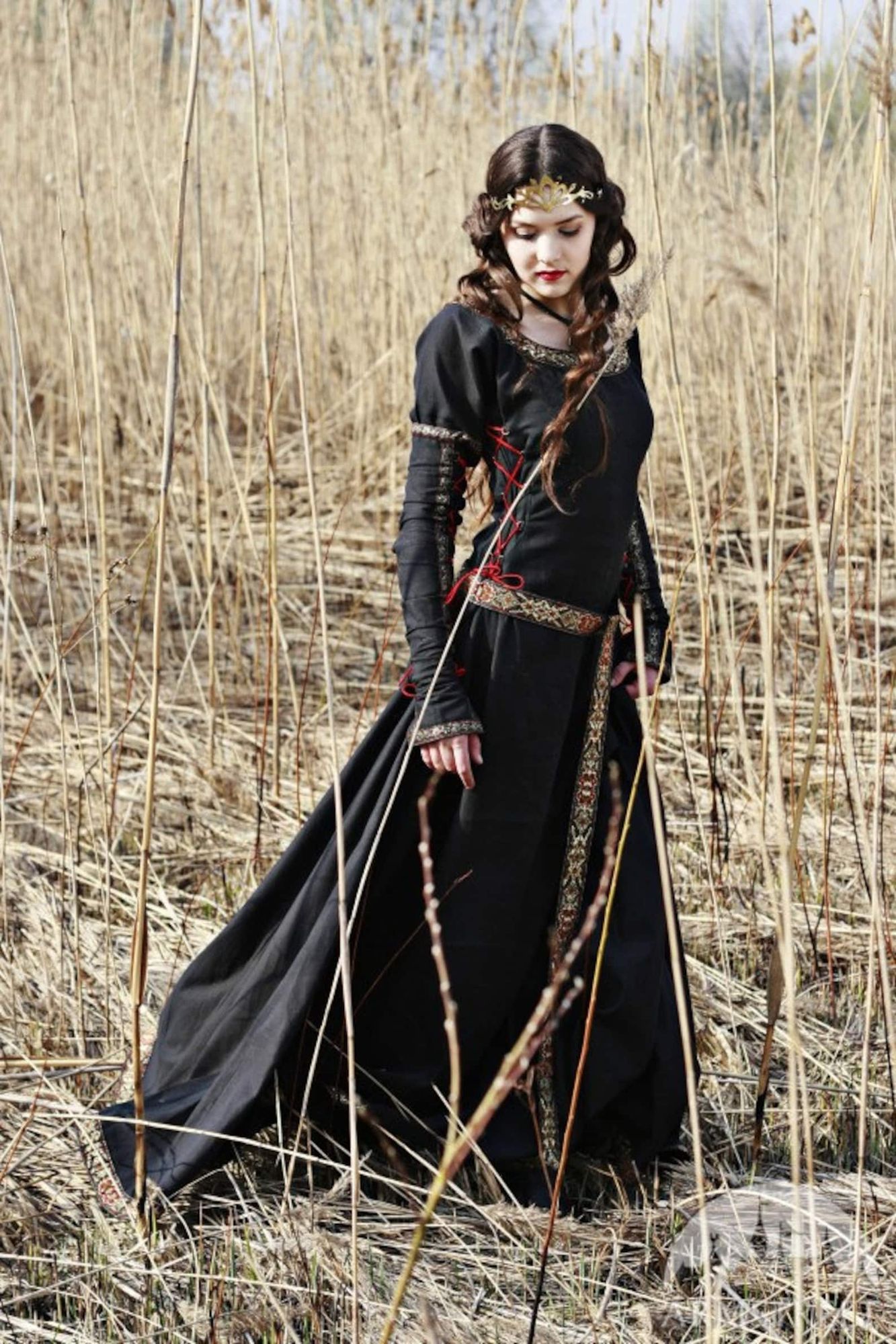 A young brunette lady wearing a beautiful medieval black dress with embroideries in a medieval landscape.