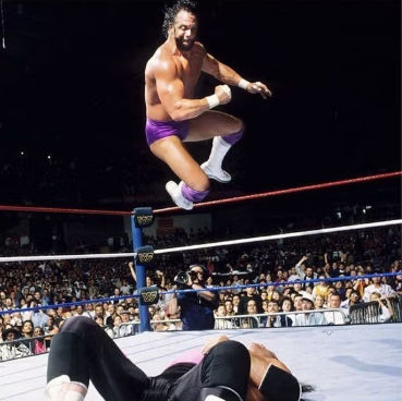 Reimagine this image by replacing the wrestler laying on the mat with a zombie in tattered clothing. The zombie on the mat should look like...