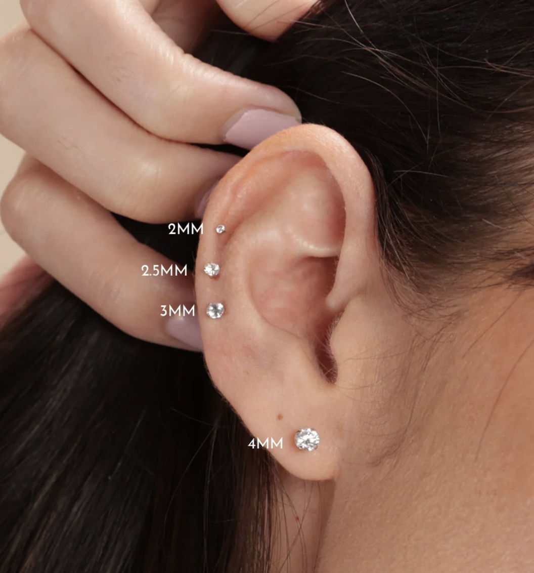 A side profile of a women pulling hair back revealing a pierced ear . Her nails have space theme and stars, galaxy in the background. the im...