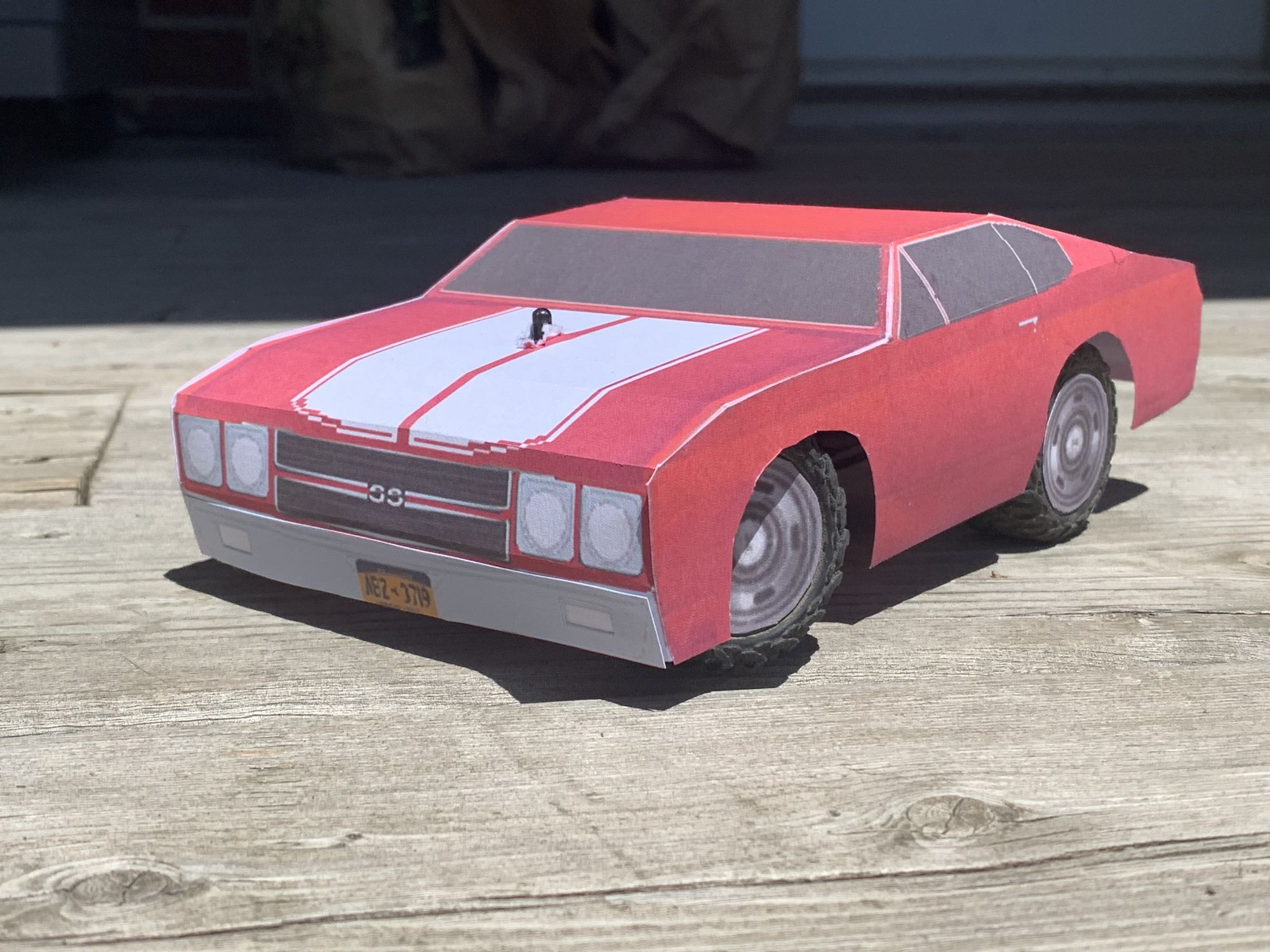 Red Chibi 1970 Chevelle with white stripes driving on a dirt road